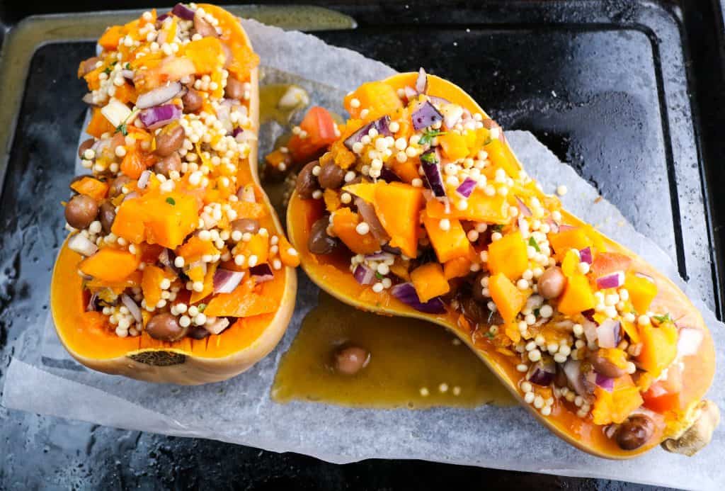 le due metà della zucca butternut ripiene di cous cous gigante e verdure su una teglia da forno prima della cottura