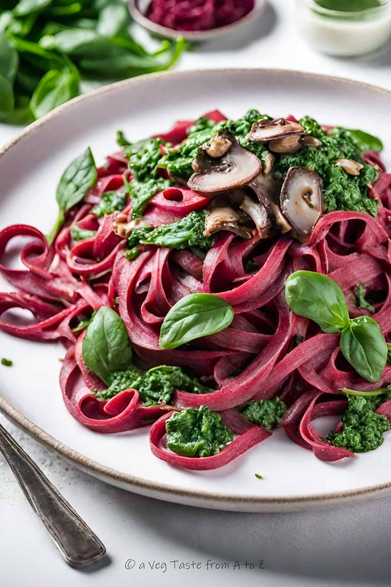 beetroot tagliatelle with brown mushrooms and spinach leaves and pesto, on light plate with white background close up side