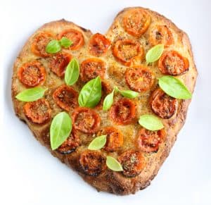 Focaccia a forma di cuore con pomodorini e basilico fresco.