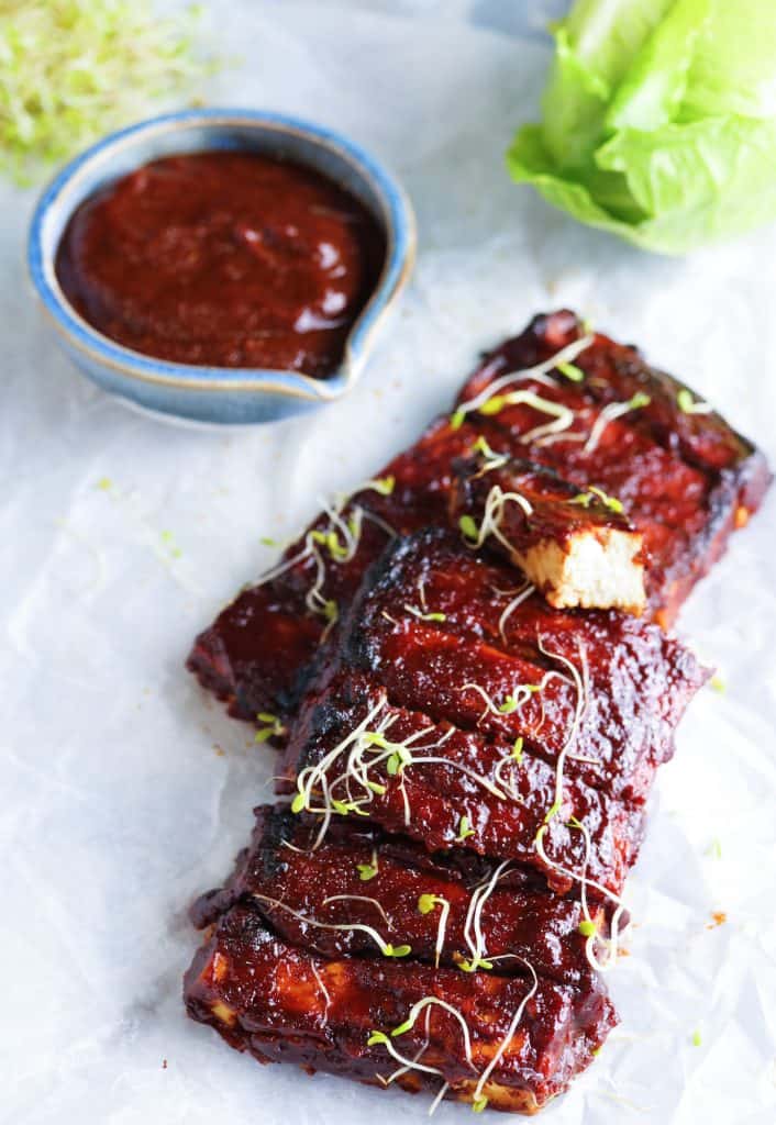 cut piece of tofu laying over the Tofu Ribs with Homemade Spicy BBQ Sauce topped with alpha-alpha sprouts