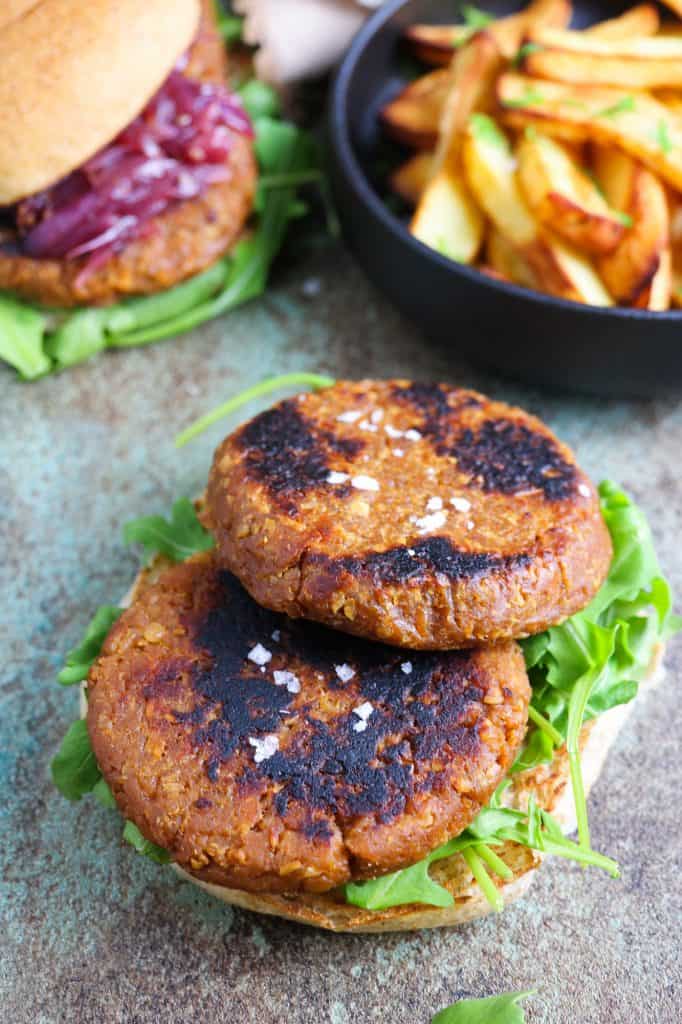 Vegan burgers patties made of soy TVP and gluten with oven baked chips on a side and a burger on the background
