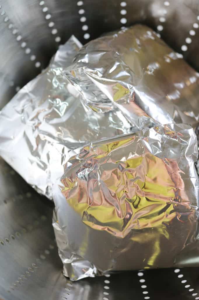 vegan burgers wrapped in foil and arranged into a colander before steaming