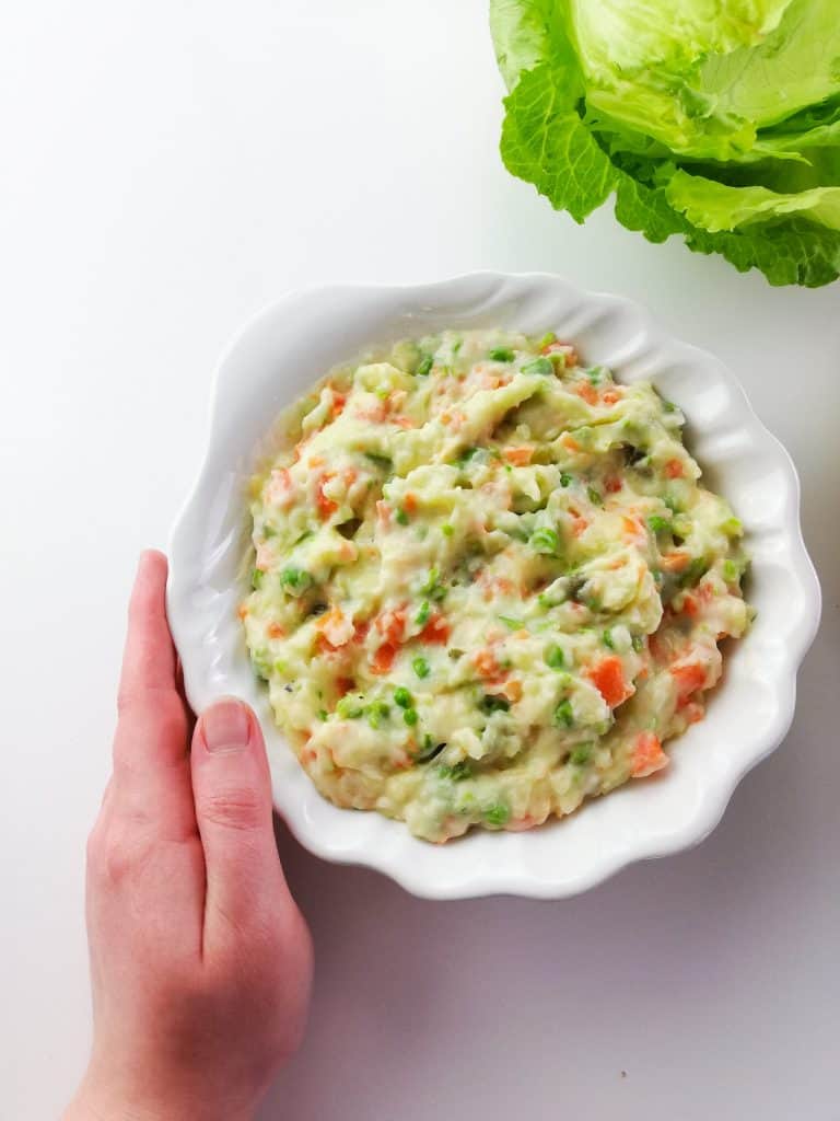 vegan russian salad with hand holding the plate