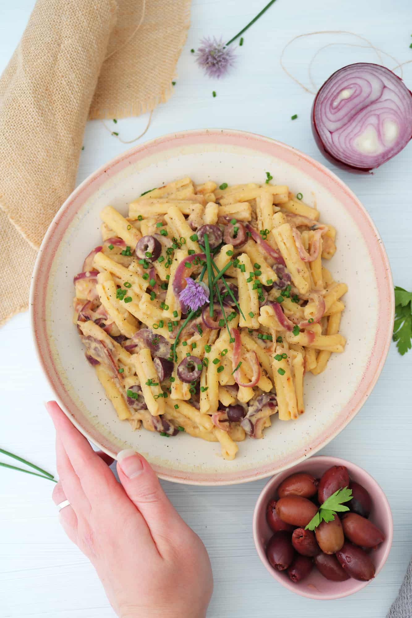 Hummus Pasta Olive and Caramelized Onion hand holding plate