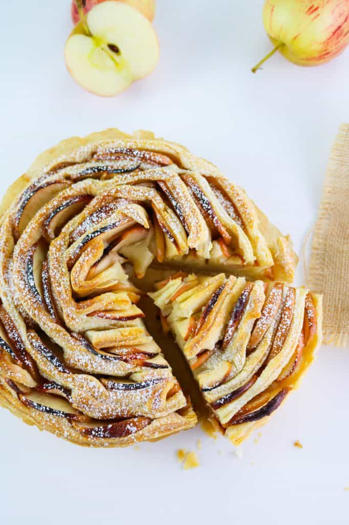 apple flaky tart presented with icing sugar and apples on white table