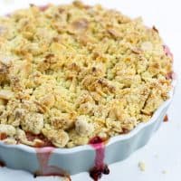 Amaretto & Rhubarb crumble on a grey, round ceramic dish on a white surface with almond shavings close up for feature image