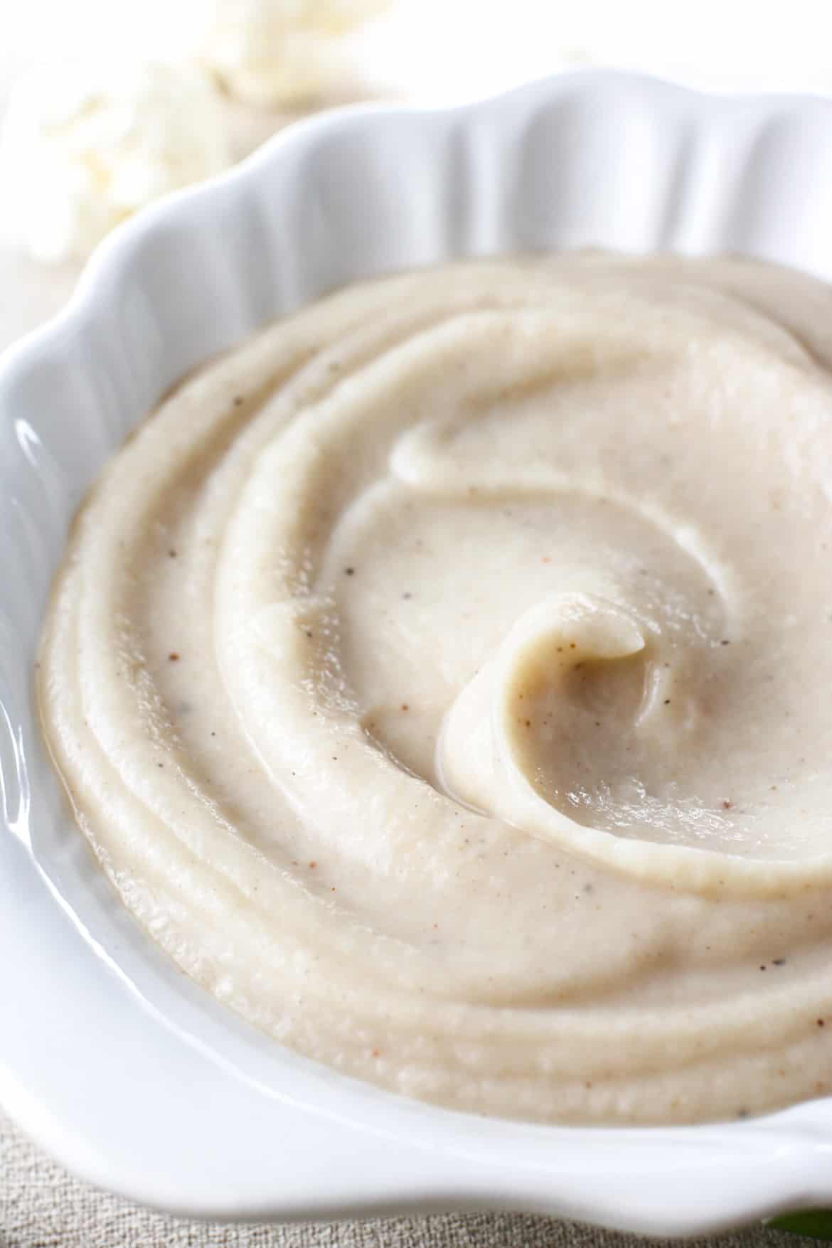 silky smooth vegan cauliflower alfredo sauce in a shell themed white bowl with a swirl on top