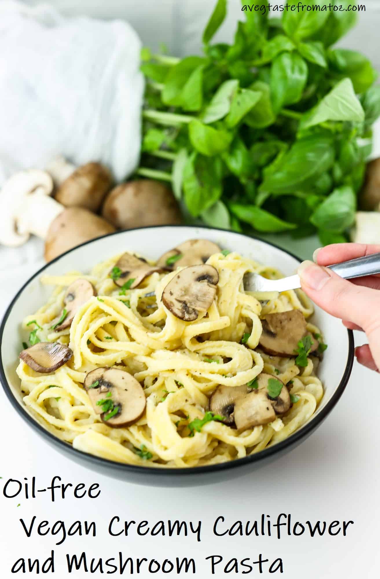 Vegan Creamy Cauliflower and Mushroom Pasta in a white bowl, right hand with a fork twisting spaghetti with raw mushrooms and basil on the background with text to be shared on Pinterest