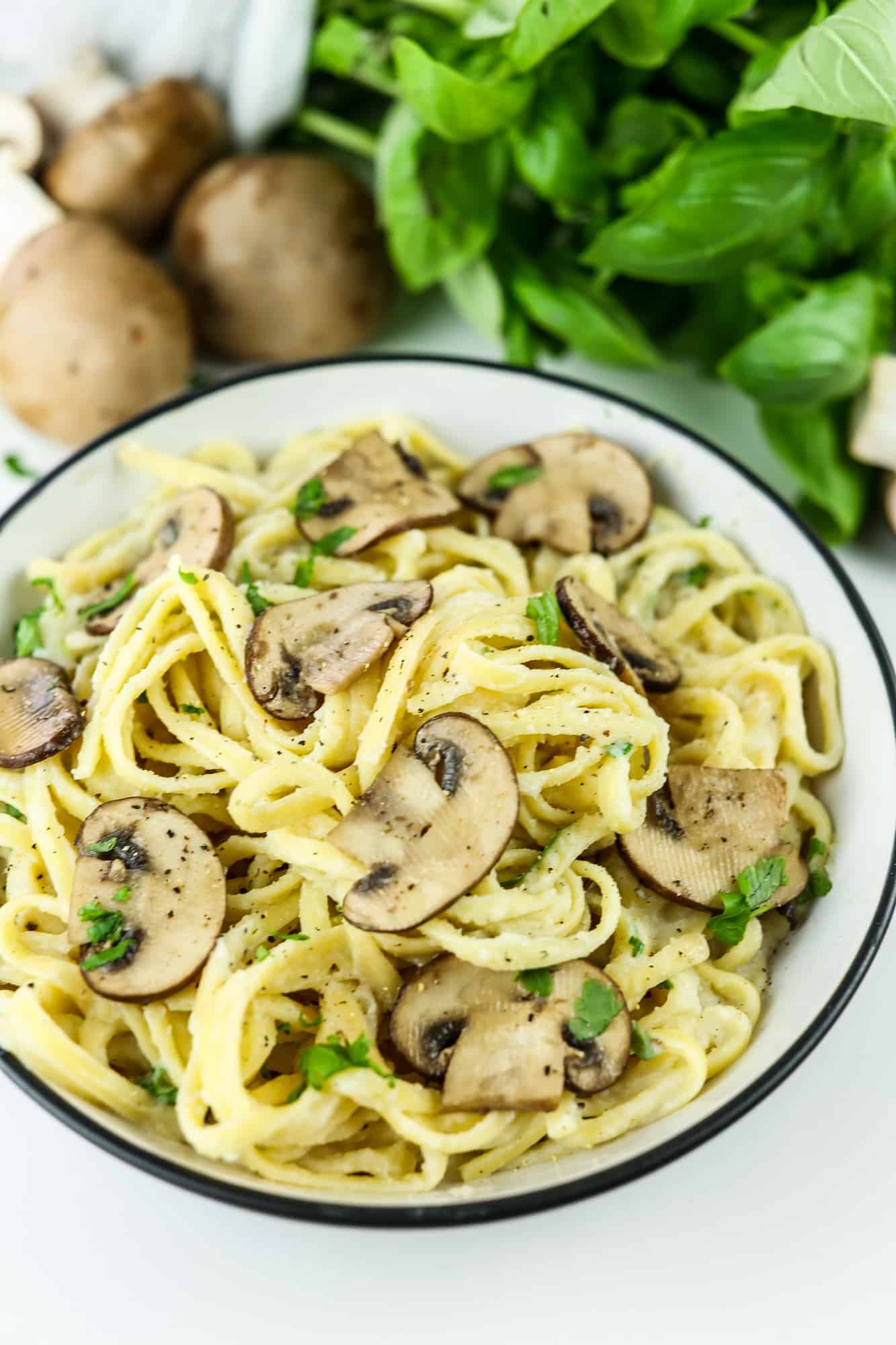 Vegan Creamy Cauliflower and Mushroom Pasta in a white bowl with raw mushrooms and basil on the background close up on the plate different angle