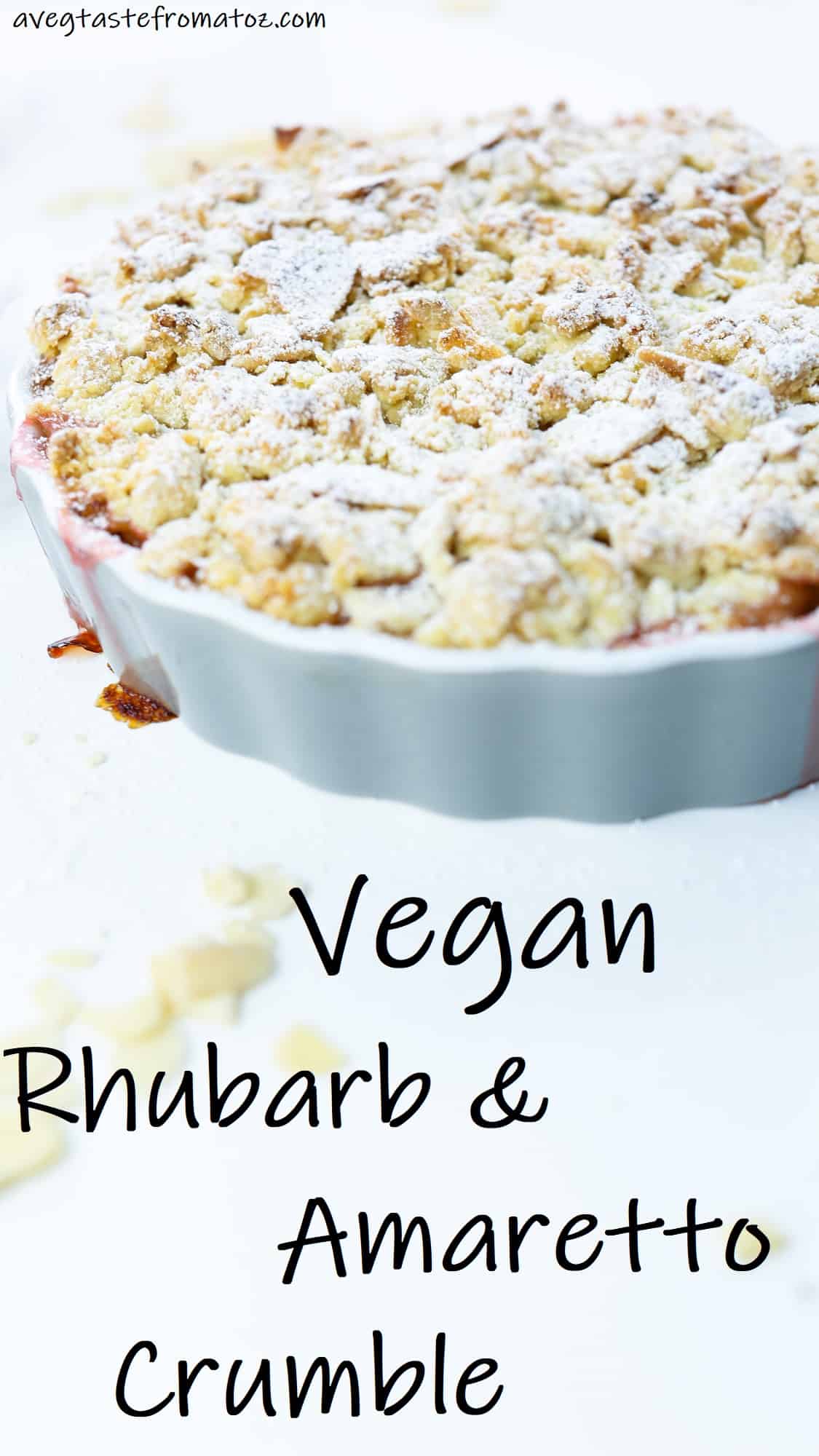 image with text of the vegan Amaretto & Rhubarb crumble on a grey, round ceramic dish on a white surface with almond shavings