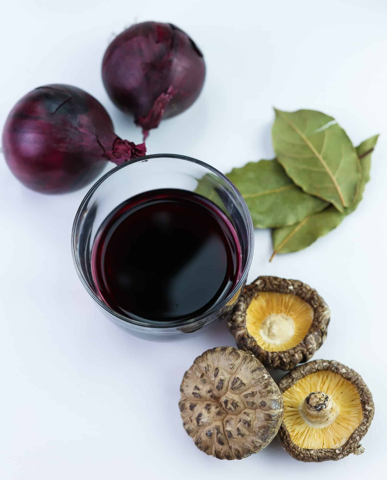 red wine, red onions, bay leaves and shiitake mushrooms on white board