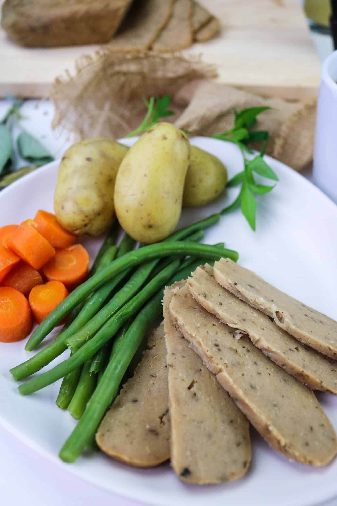 Turkey(less) loaf, vegan and gluten free meat alternative sliced on a plate with steamed vegetables
