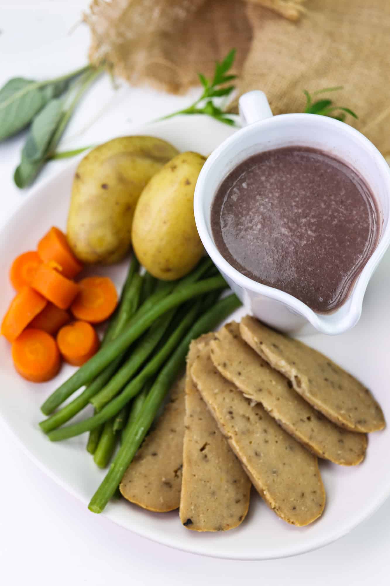 Turkey(less) loaf, vegan and gluten free meat alternative sliced on a plate with steamed vegetables and gravy pot