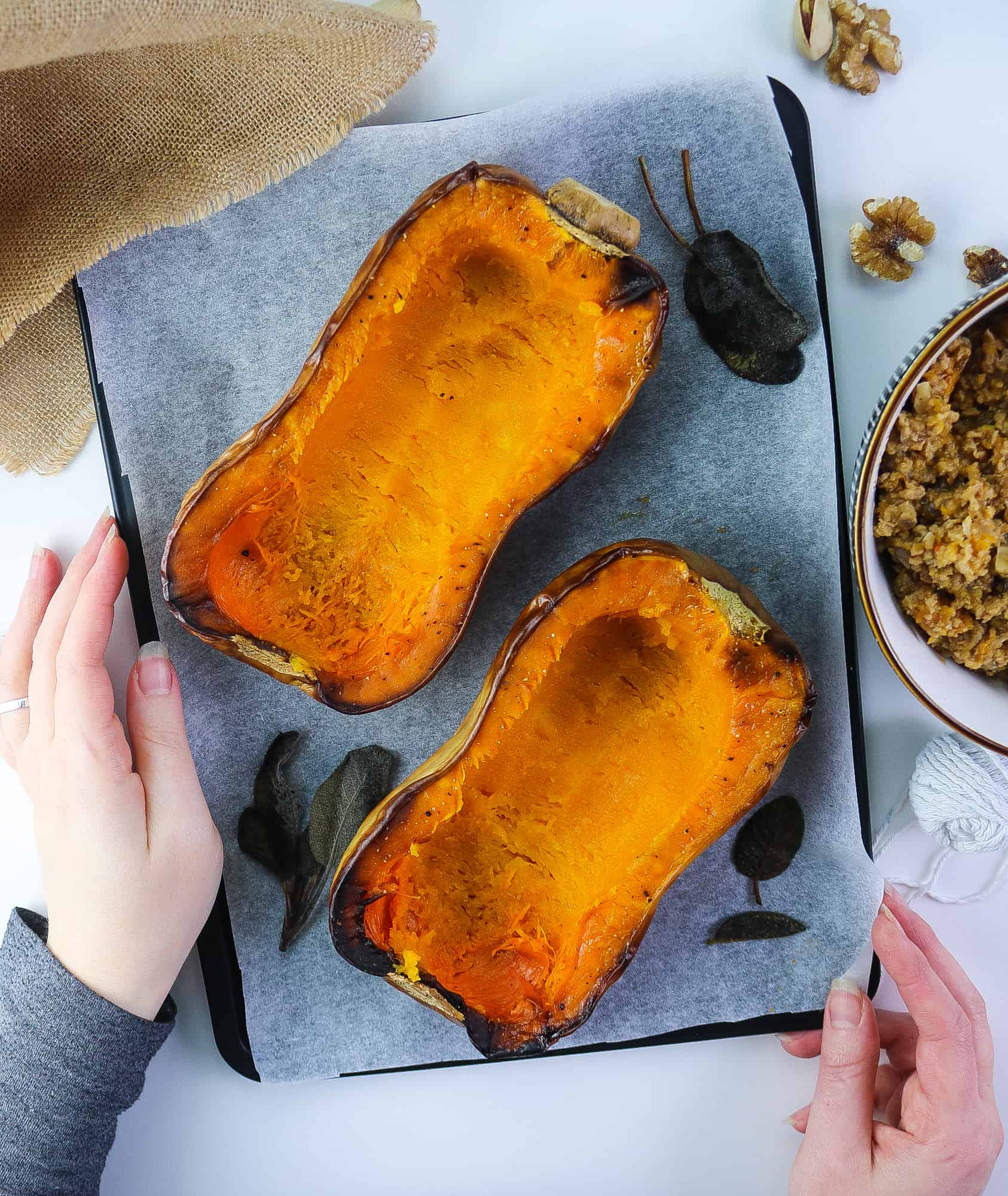 Scooped Roasted Butternut squash with fresh sage leaves on a oven tray and hands holding it