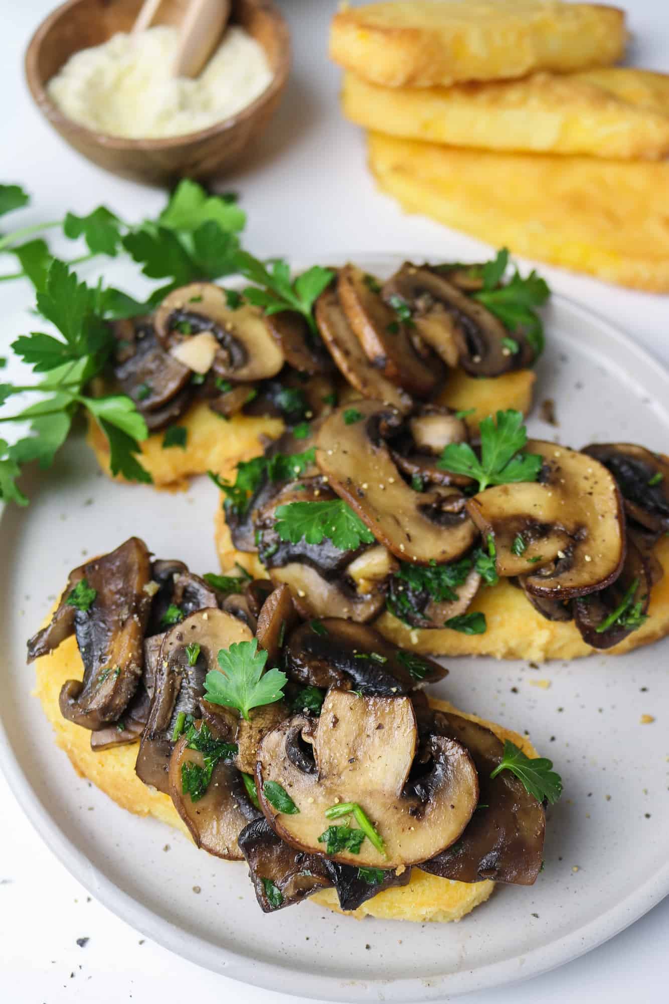 3 bruschetta polenta on a white plate with air fried polenta slices and semolina flour in the background