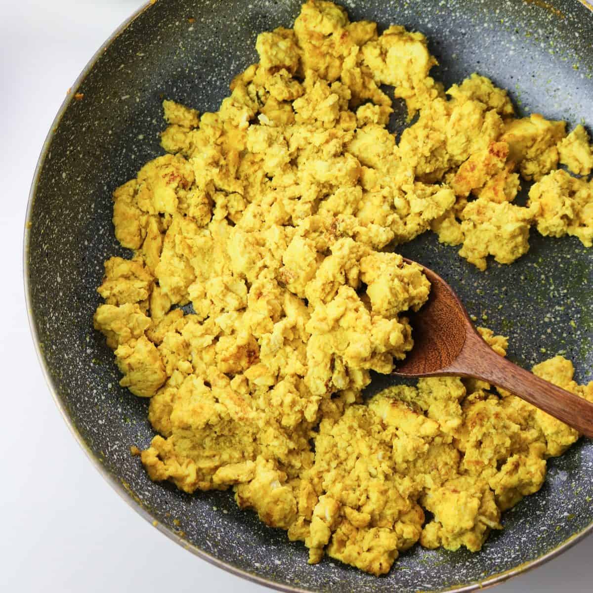 vegan scrambled tofu in a pan with a wooden spoon