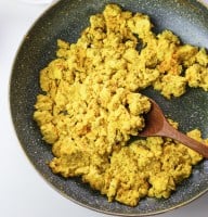 vegan scrambled tofu in a pan with a wooden spoon