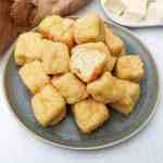 fluffy deep fried soft tofu cubes with one cut in half showing the interior on a grey plate