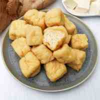 fluffy deep fried soft tofu cubes with one cut in half showing the interior on a grey plate