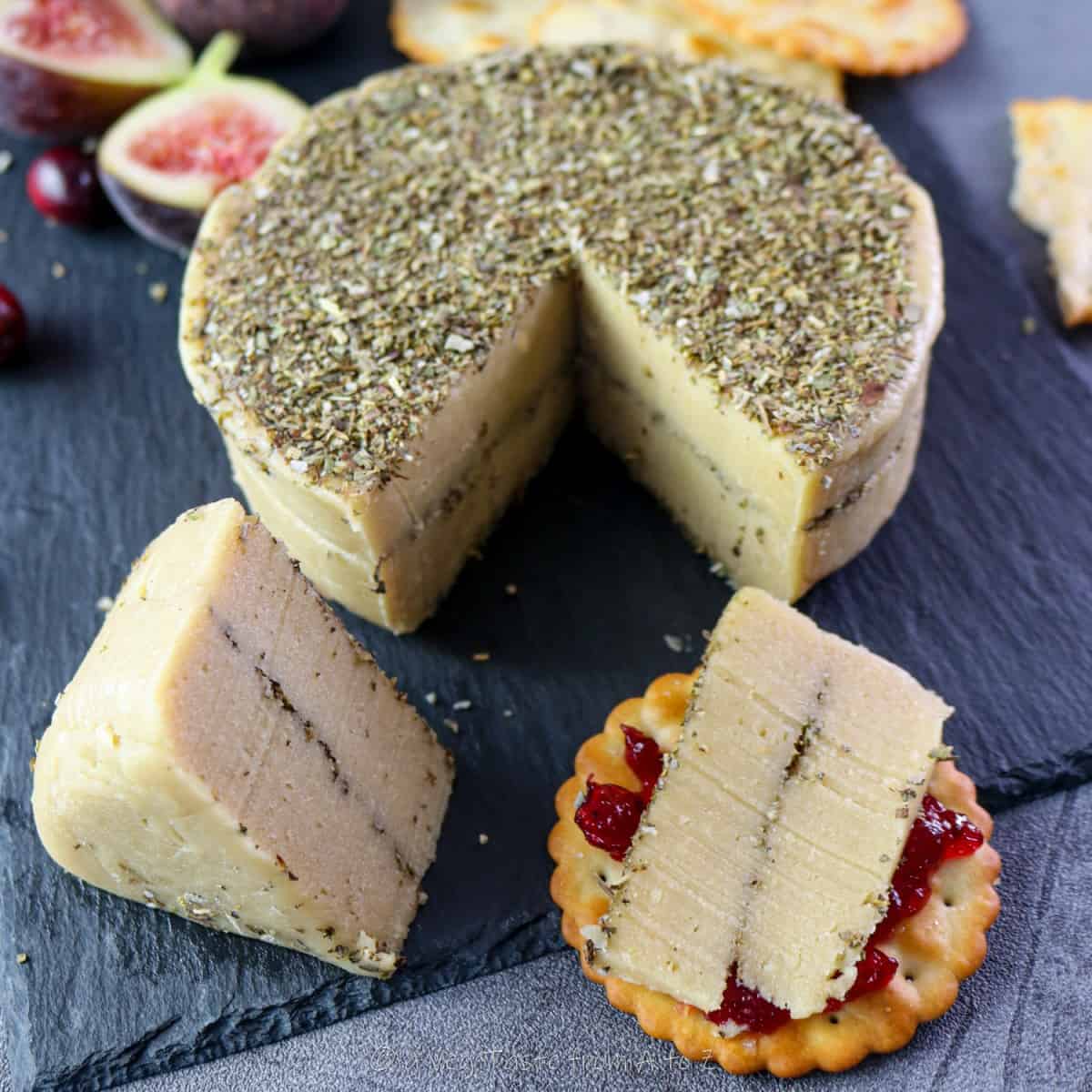 cashews vegan cheese block with dried herbs and slices on black board