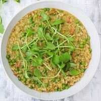 risi e bisi in a white plate topped with pea shoots