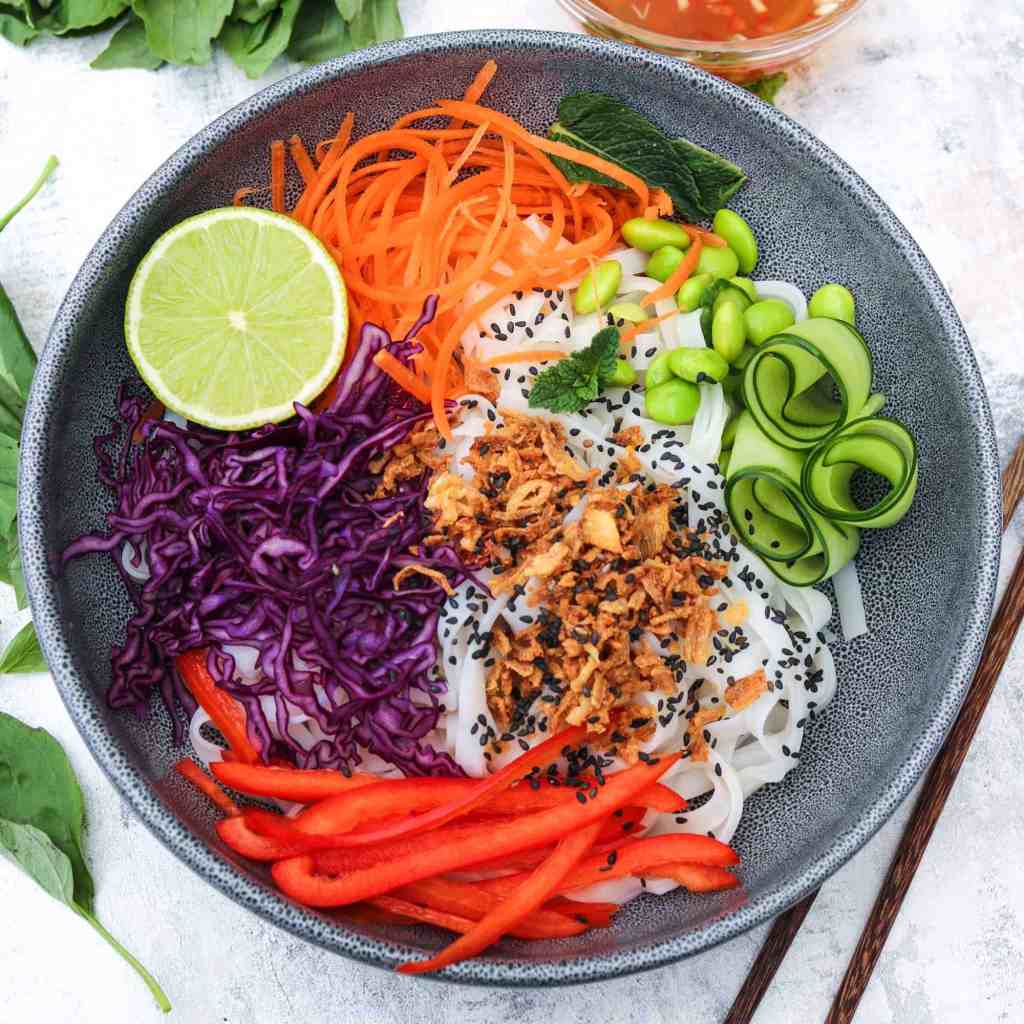 crice noodles with seasonable colourful vegetables in a grey plate with half a lime
