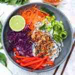 crice noodles with seasonable colourful vegetables in a grey plate with half a lime
