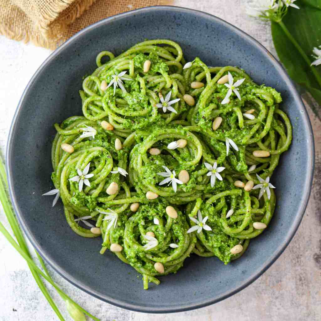 wild garlic pesto spaghetti rolled into nests served on a grey plate and topped with pine nuts and wild garlic flowers