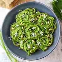 wild garlic pesto spaghetti rolled into nests served on a grey plate and topped with pine nuts and wild garlic flowers