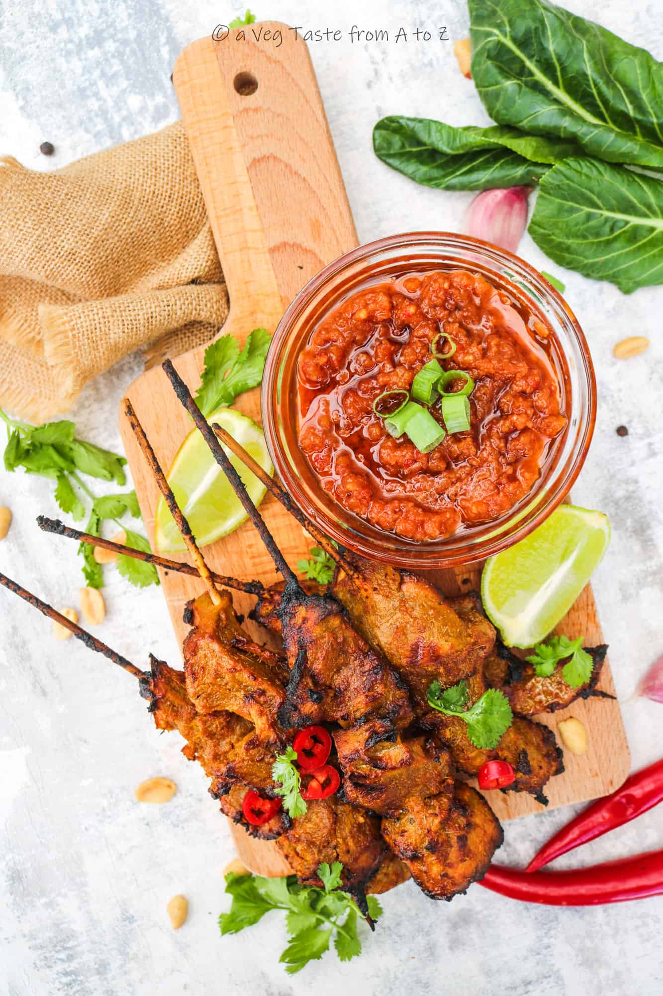 vegan satay chicken on a wooden board with a bowl of peanut satay sauce garnished with cilantro, chilli, peanuts and lime wedges