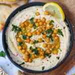 creamy homemade hummus in a black bowl with roasted chickpeas and herbs