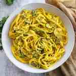 linguine pasta coated in saffron creamy sauce and roasted zucchini slices arranged in a white plate and top down shot