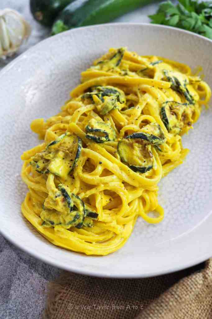 linguine pasta coated in saffron creamy sauce and roasted zucchini slices arranged in a white plate