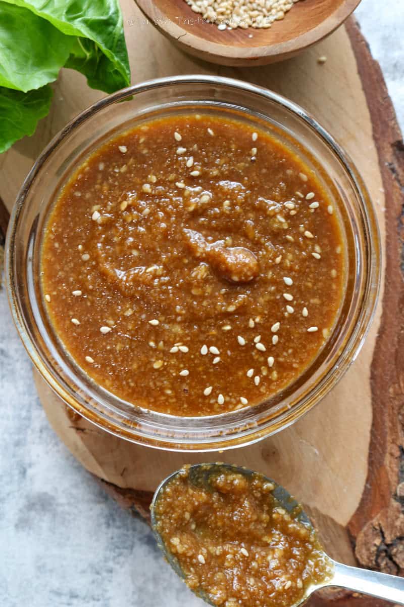sesame and miso dressing in a small glass bowl over a wooden board with sesame seeds and salad props