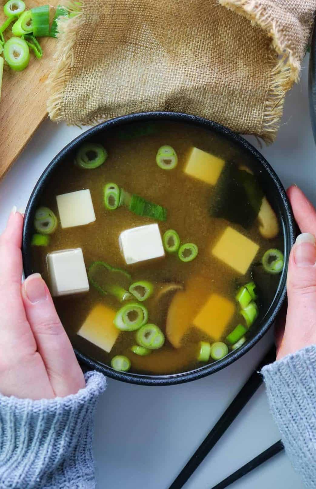 vegan miso soup in a black bowl hold by hands