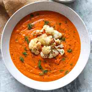 vibrant orange roasted cauliflower soup in a white dish topped with roasted cauliflower florets, black pepper and fresh dill