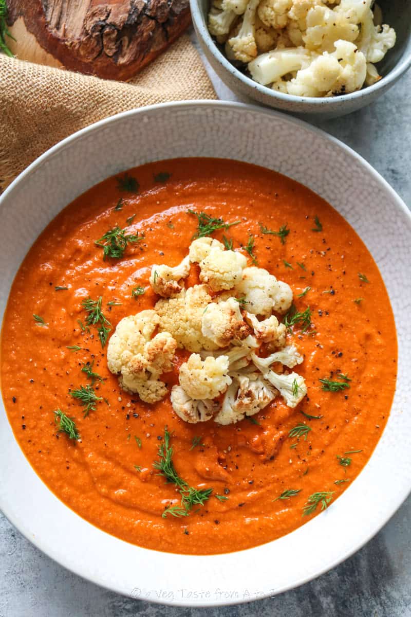 vibrant orange roasted cauliflower soup in a white dish topped with roasted cauliflower florets, black pepper and fresh dill