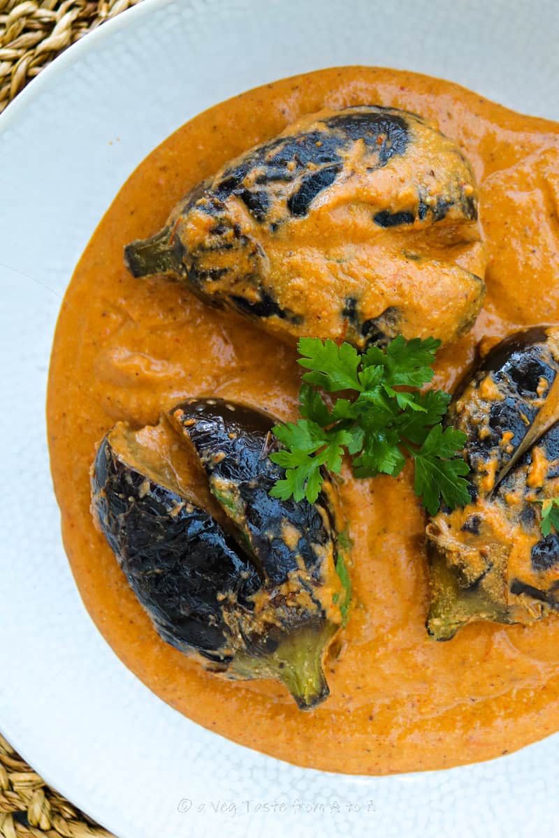 close up to Bagara Baingan in a serving plate in bright orange gravy garnished with fresh coriander