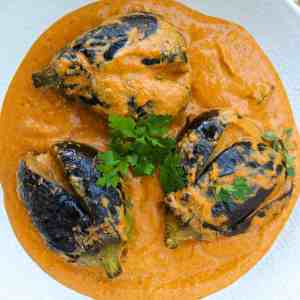 Bagara Baingan in a serving plate in bright orange gravy garnished with fresh coriander